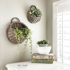 two wicker baskets are hanging on the wall above a table with books and plants