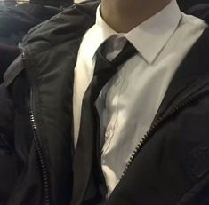 a man wearing a jacket and tie sitting on a train seat with his hands in his pockets