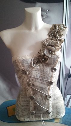 a mannequin made out of newspaper with flowers on the top and buttons attached to it