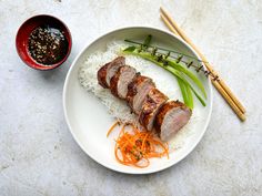 a white plate topped with meat and veggies next to a bowl of sauce