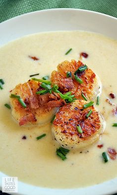 two scallops sit on top of some soup in a white bowl with green onions