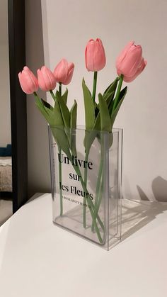 three pink flowers in a clear vase on a white table with the words innuve surres des fierts