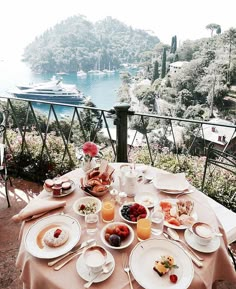 the table is set with breakfast food and drinks on it, overlooking the water's edge