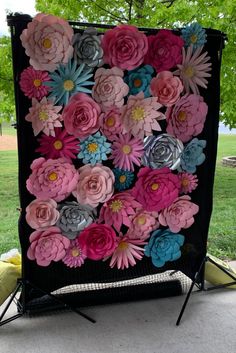 a black backdrop with pink, blue and grey flowers on it in front of a tree