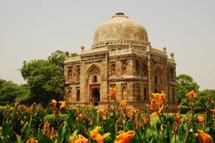 an old building surrounded by flowers in the middle of a field with trees and bushes