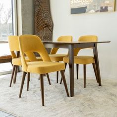 a dining room table with yellow chairs in front of a large window and artwork on the wall