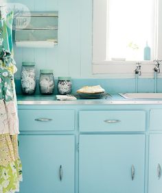 a kitchen with blue cabinets and white counter tops in front of a window that is open