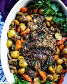 a white bowl filled with meat, potatoes and carrots on top of a blue table cloth