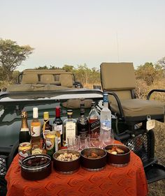 an outdoor picnic table with drinks and snacks on it in front of a safari vehicle