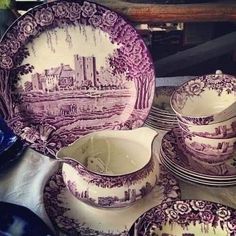 a table topped with lots of purple and white china dishes on top of each other