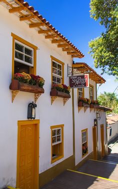 a white building with yellow shutters and flower boxes on the outside wall, along side a sidewalk