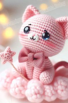 a pink knitted cat figurine sitting on top of a white surface with lights in the background