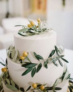 a three tiered cake with olives and leaves on the top is sitting on a table