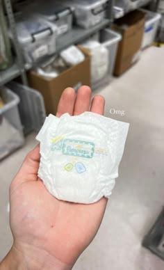 a hand holding a white cloth diaper in front of shelves with boxes and other items