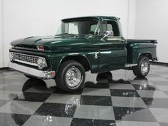 an old green truck is parked on a checkered floor