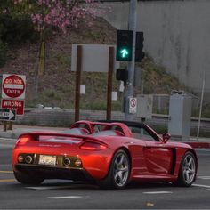 a red sports car driving down the road next to a stop light and street sign