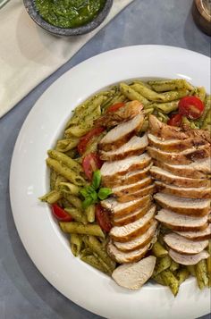 a white plate topped with green beans and sliced chicken next to a bowl of pesto sauce