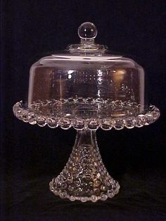 a clear glass cake dish with a domed cover on the top and bottom, sitting on a black surface