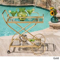 a gold serving cart next to a pool with flowers and vases on the table