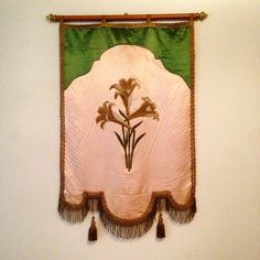 a wall hanging with flowers and tassels on it's side in a room