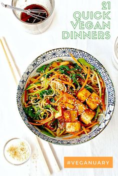 a bowl filled with noodles and vegetables next to chopsticks on a white table