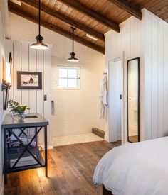 a bedroom with white walls and wood floors, along with an open door leading to the bathroom