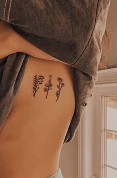 a woman's back with three small tattoos on her left side, and flowers in the middle