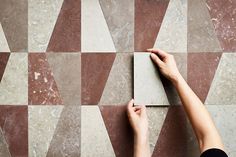 a person's hand reaching for a tile on a wall with geometric design in the background