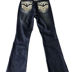 Dark Blue Jeans With Faded Design On The Front And Back Of The Legs. There Are Clear Rhinestones At The Front Pockets And A Silver With Clear Rhinestone Button At The Waist. White Stitching Throughout The Seams. The Back Pockets Have White, Beige And Metallic Silver Embroidered Designs Embellished With Clear Rhinestones And Silver Studs. 85% Cotton, 4% Rayon, 6% Polyester, 5% Spandex. Angel Jeans Los Angeles Brand. Boot Cut Style. Size 11/28. Measurements: Waist Lying Flat 14”, Rise 10”, Inseam Angel Jeans, Angels Jeans, 2000s Clothes, Character Board, Embroidered Designs, Jeans Dark Wash, Dark Blue Jeans, Virtual Closet, Pocket Jeans