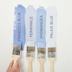 three paintbrushes with different shades of blue and white painted on them, one being held by a hand