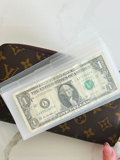 a person holding a fake one dollar bill in front of a purse on a table