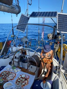 a woman sitting at the helm of a boat with pizza and drinks on the table