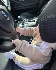 a baby sitting in the driver's seat of a car wearing a beanie