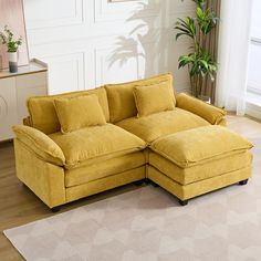 a living room with a large yellow sectional couch and potted plant in the corner