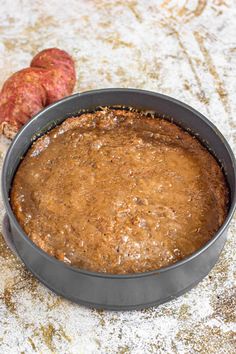 a cake pan filled with brown batter next to two sweet potatoes on top of a table