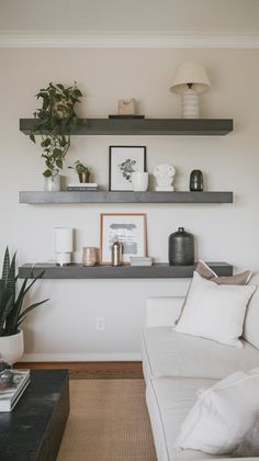 a living room filled with white furniture and lots of shelves above the couch, along with potted plants