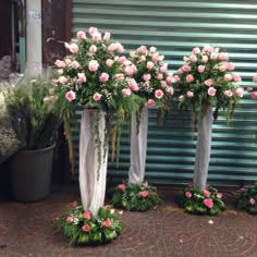 three tall vases with pink roses and greenery on the side of a building