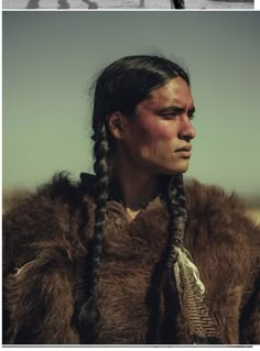 a man with long hair and braids in a fur coat looking off into the distance