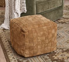 a square footstool sitting on top of a rug next to a green couch