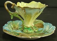 a green and yellow vase sitting on top of a leafy saucer with gold trim