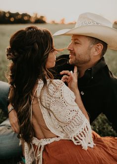 a man and woman are sitting on the ground together, one is wearing a cowboy hat