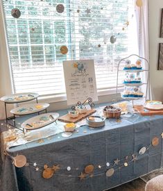 a blue table topped with lots of desserts next to a window covered in curtains