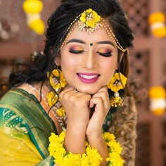 a woman with yellow flowers in her hair posing for the camera while wearing a green and yellow saree