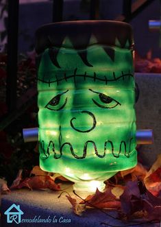 a lighted jar with a face on it sitting in front of some leaves and plants