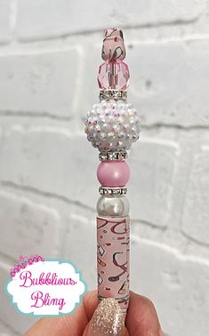 a hand holding a pink and white beaded pen