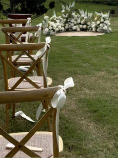 four wooden chairs with bows on them sitting in the middle of a grassy area next to flowers