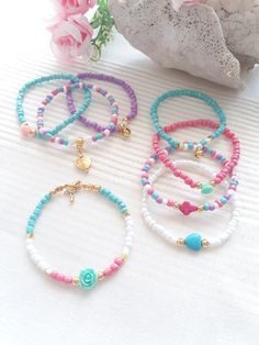 three bracelets with beads and charms on top of a white table next to pink flowers