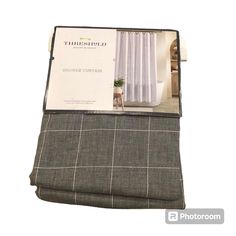 the inside of a folded book on top of a gray plaid bed sheet with white curtains