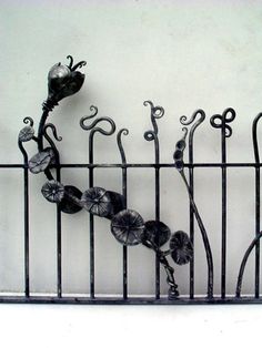 an iron fence with flowers and leaves on it's sides, against a white wall