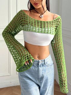 a woman wearing jeans and a crop top with crochet on the shoulders, standing in front of a white wall